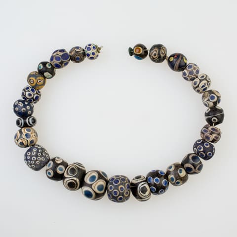 A string of 27 glass eye beads laid in an open loop: dark blue and black
                           beads spotted with white, blue and yellow eyes.